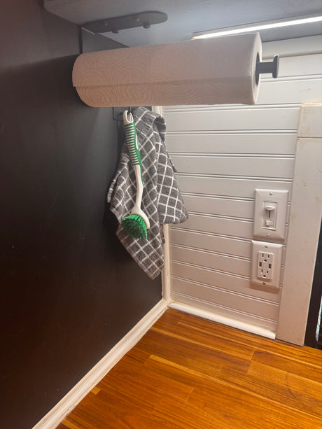 RV rental detail: convenient paper towel roll, hanging brush, and modern outlets, set against contrasting walls & wood floor.