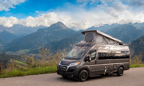 Modern grey camper van (RV rental) with pop-top tent on a scenic mountain road, perfect for nature adventures.