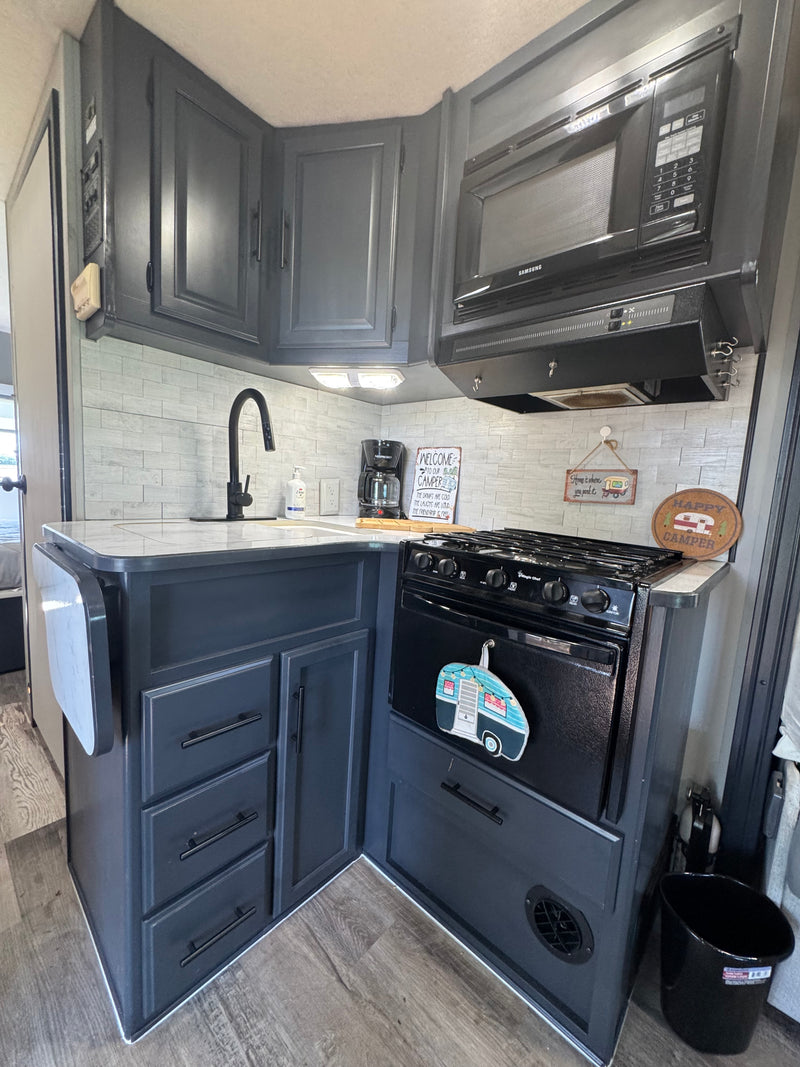 Stylish gray RV rental kitchen: Samsung microwave, Magic Chef stove, sink, coffee maker, tile backsplash, and a handy pull-out counter. — photo 9