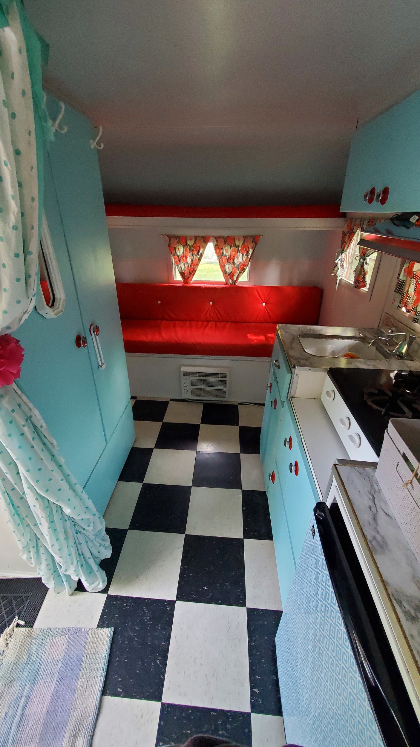Cozy retro RV rental interior with vibrant red seating, a checkerboard floor, and a teal kitchenette.