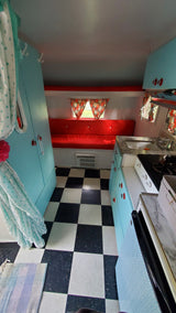 Cozy retro RV rental interior with vibrant red seating, a checkerboard floor, and a teal kitchenette.