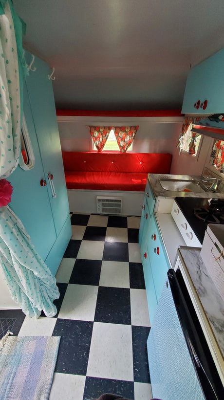 Cozy retro RV rental interior with vibrant red seating, a checkerboard floor, and a teal kitchenette.