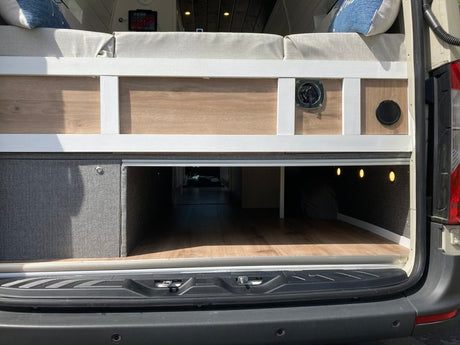 Spacious RV rental interior features a custom bed platform with under-bed storage, built-in cabinet, and warm lighting.