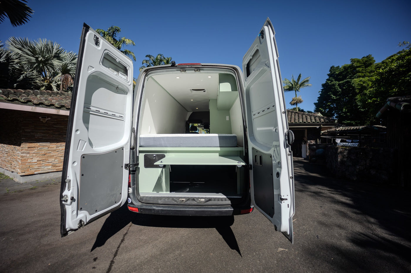 RV rental: Bright custom camper van interior visible from open rear doors, featuring a bed and storage. — photo 12