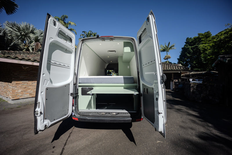 RV rental: Bright custom camper van interior visible from open rear doors, featuring a bed and storage. — photo 12