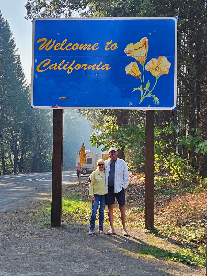A couple greets California under a poppy welcome sign, with an RV signaling an ideal RV rental adventure ahead.