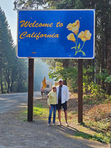 A couple greets California under a poppy welcome sign, with an RV signaling an ideal RV rental adventure ahead.