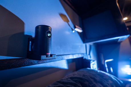 Compact projector on a shelf, providing entertainment in an RV rental. Blue ambient light creates a cozy vibe.
