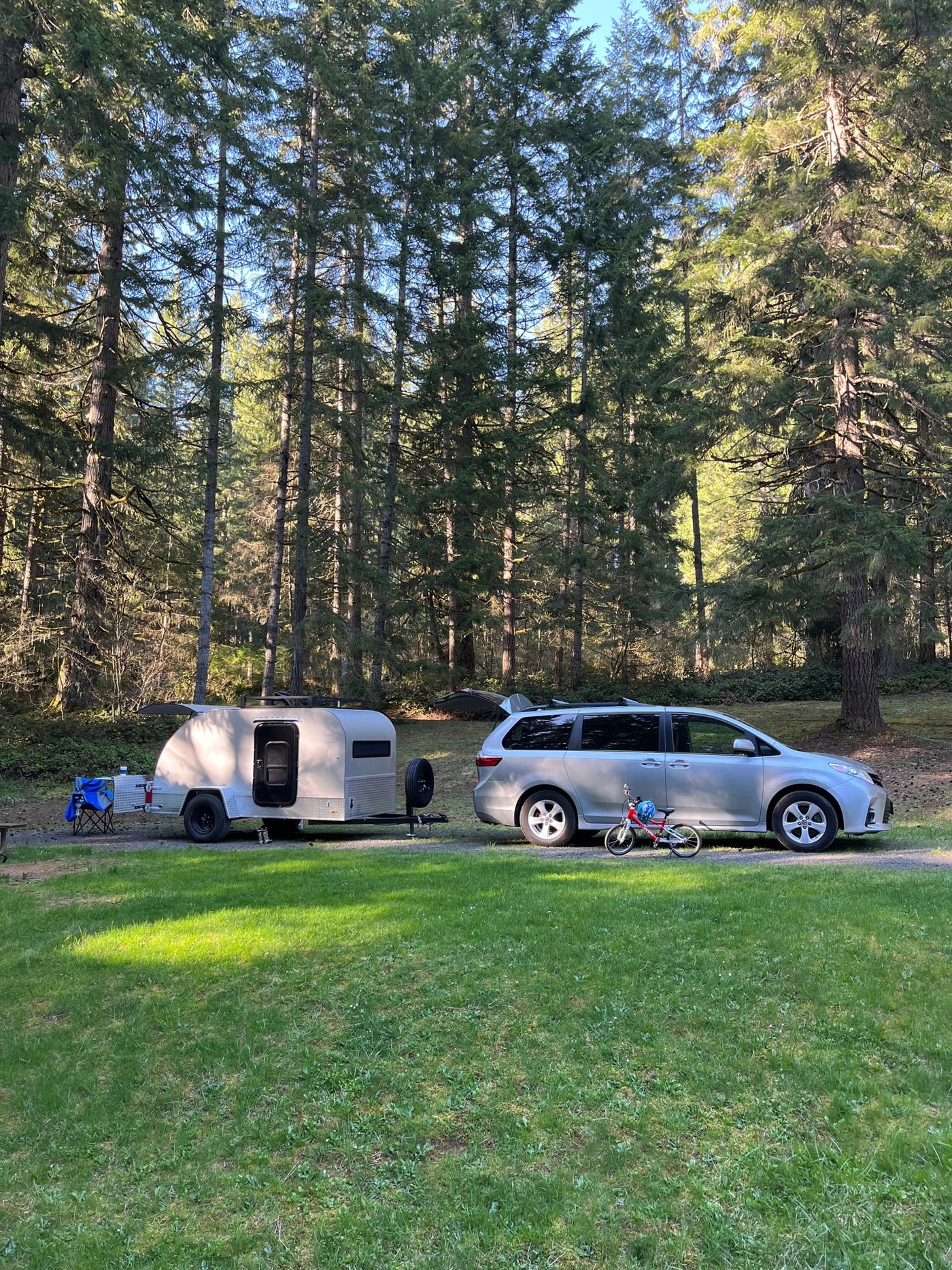  a child visible inside. Scenic rocky landscape in background.|Silver minivan with rooftop cargo box and an attached teardrop RV rental trailer — photo 2
