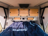 Cozy RV rental interior featuring a comfortable bed and overhead storage units, ready for your travels.