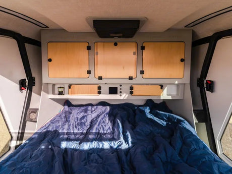 Cozy RV rental interior featuring a comfortable bed and overhead storage units, ready for your travels.