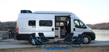 A bright Winnebago Solis RV rental parked by a lake with bikes on the rear. Camping chairs & a mat are set out.