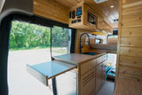 Spacious rv rental camper van interior: warm wood paneling, kitchen with sink, elevated bed, and pull-out table.