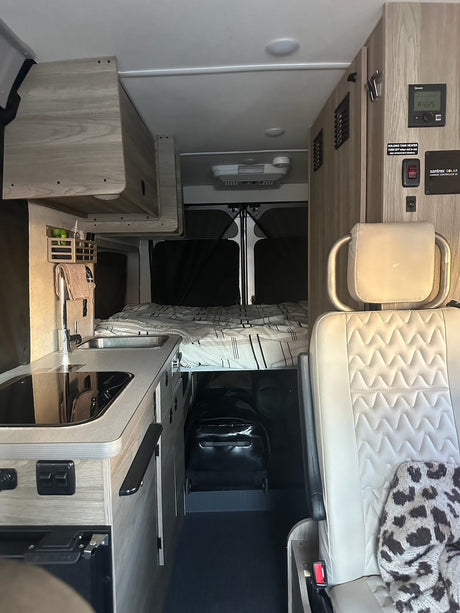 Modern rv rental interior: compact kitchen, cozy bed, passenger seat, and wall-mounted system controls.