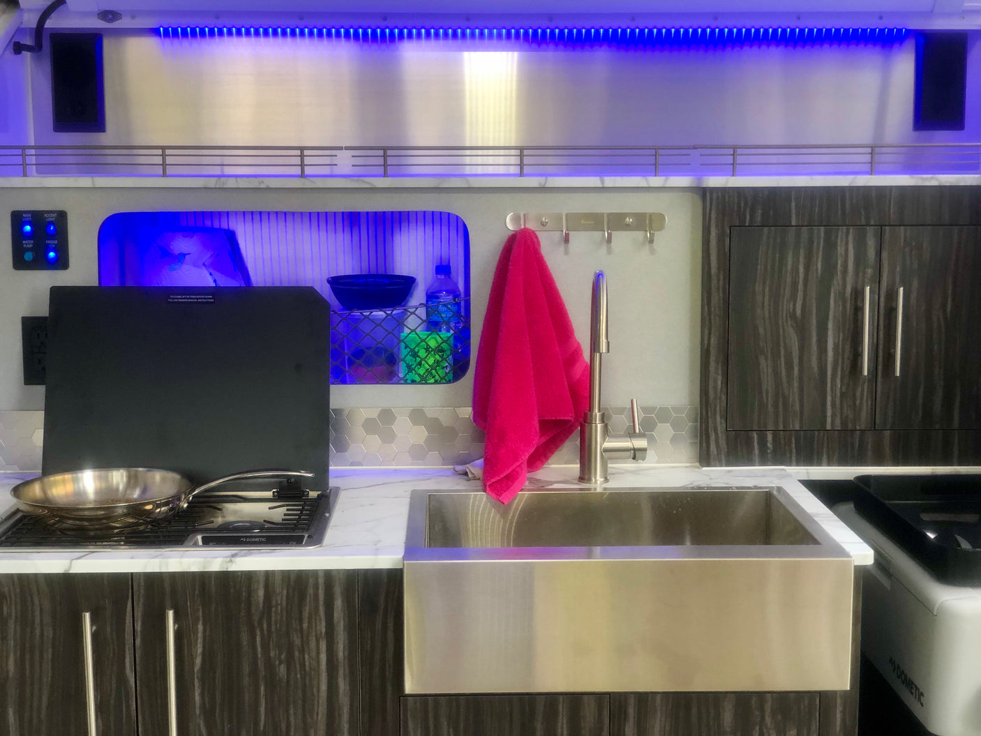 Compact RV rental kitchen with a sleek stainless steel sink, stove, dark cabinets, and blue accent lighting.