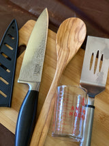 A patterned chef's knife, wooden spoon, spatula, and measuring cup on a cutting board, ideal for your RV rental kitchen.