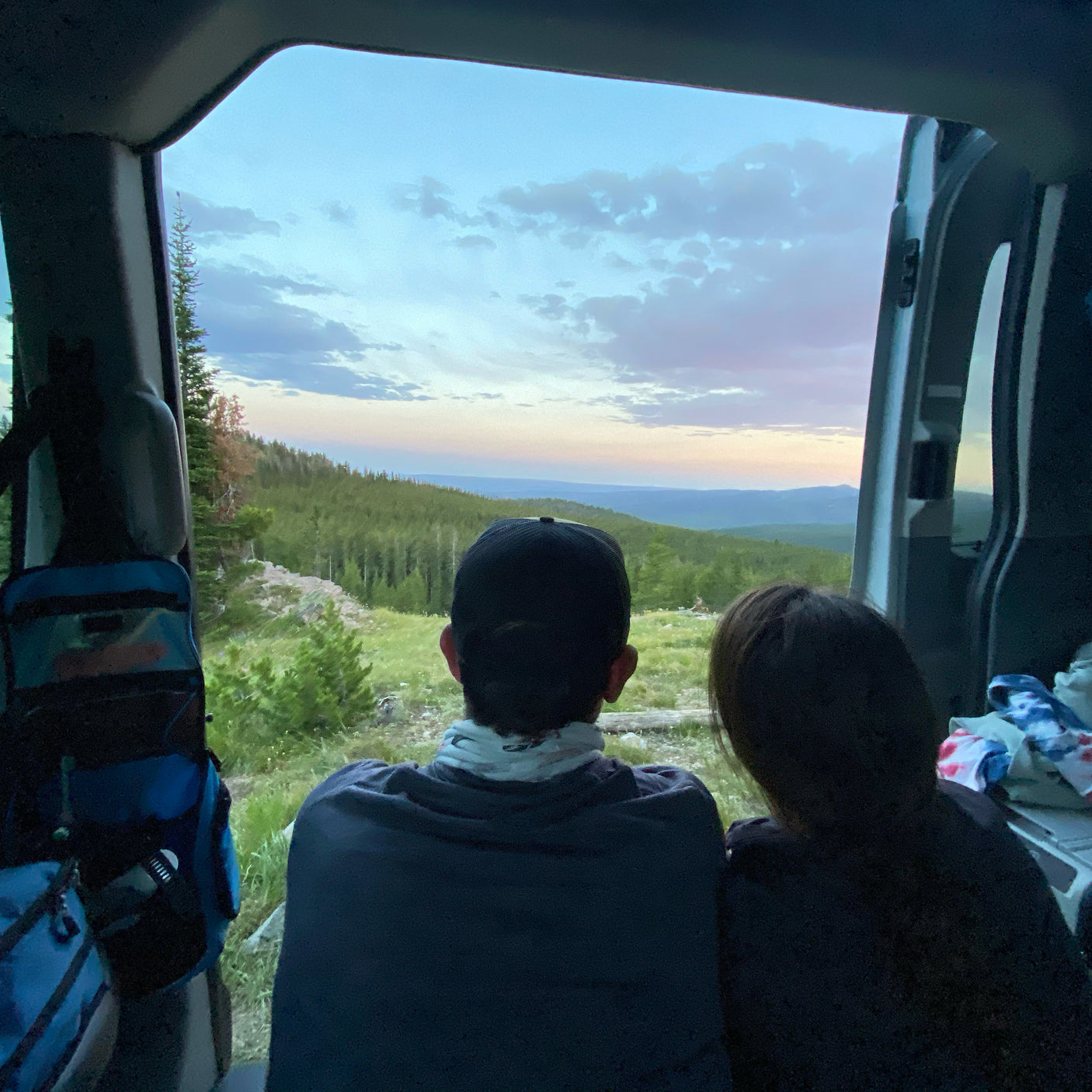 Relaxing in an RV rental, two people enjoy a beautiful mountain sunset from the vehicle's rear. Scenic view.