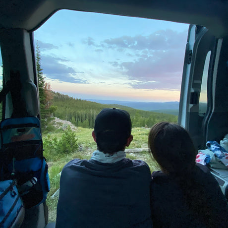 Relaxing in an RV rental, two people enjoy a beautiful mountain sunset from the vehicle's rear. Scenic view.