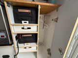 RV rental's organized storage: wooden cabinet with labeled bags, patterned drawers, a hanging rod, and a utility appliance.