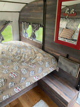 Cozy RV rental interior showcasing a bed with "Happy Camper" bedding, wood paneling, and a mirror.