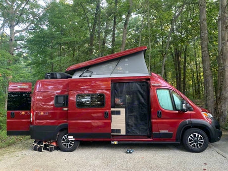 This red camper van with a pop-top roof is perfect for an rv rental adventure, parked in a serene wooded campsite.