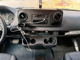 Inside an rv rental Sprinter van, this photo shows the dashboard, steering wheel, radio, cupholders, and driver's footwell.
