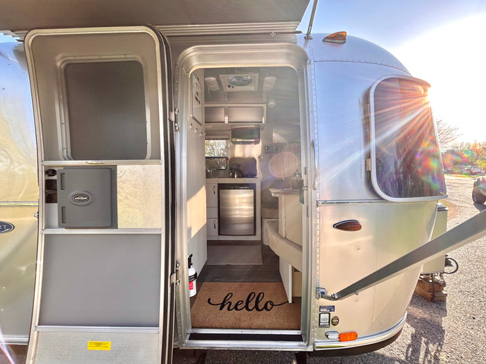 Explore a sleek Airstream travel trailer RV rental, bathed in sunlight. The open door invites you into its compact, modern interior.