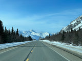 Stunning winter mountain road for your next RV rental adventure. Snow-covered peaks, evergreens, and blue skies await.