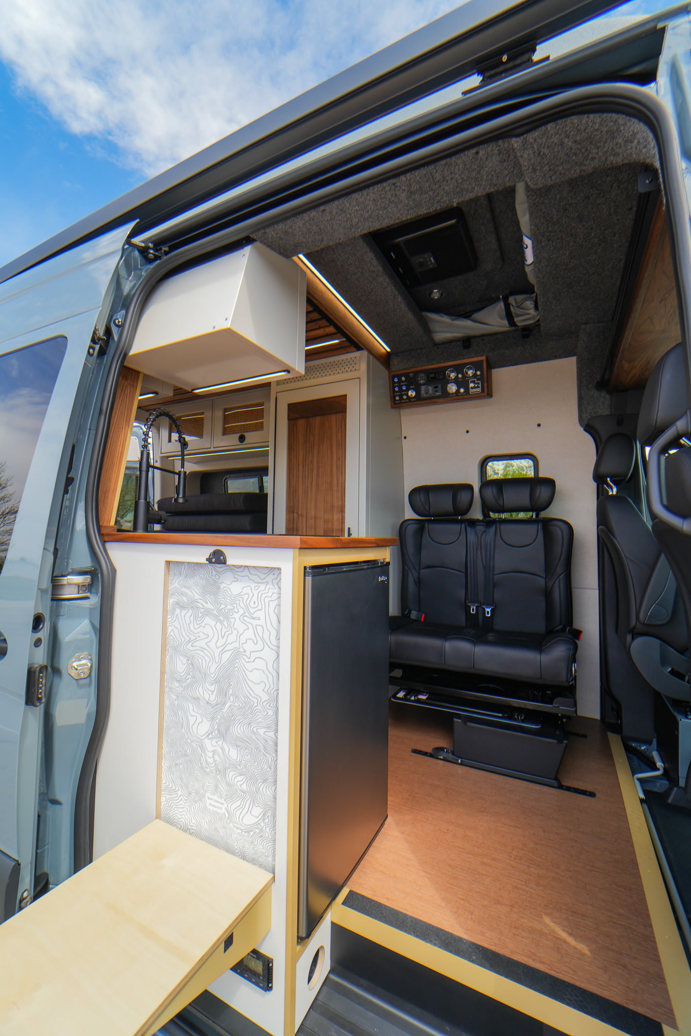 Spacious custom camper van rv rental interior featuring a kitchen, fridge, and comfortable rear seating area.