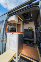 Spacious custom camper van rv rental interior featuring a kitchen, fridge, and comfortable rear seating area.