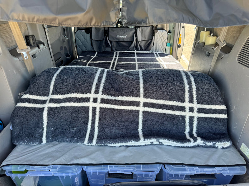 This RV rental interior features a cozy bed with a plaid blanket, storage bins, and Hanemia hanging organizers. — photo 2