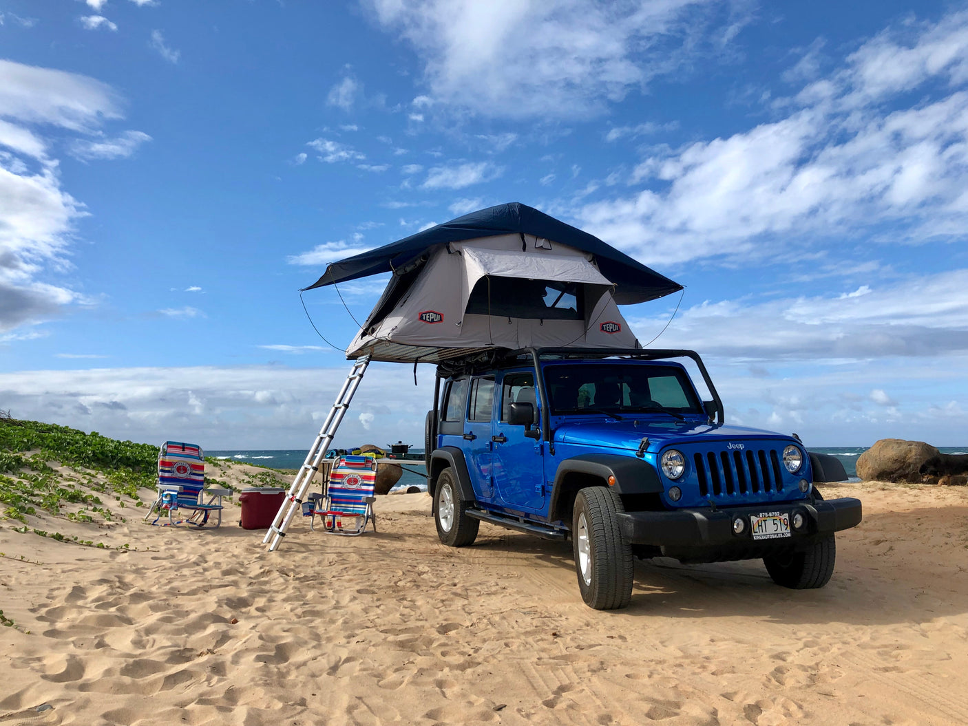 Beach camping setup with a blue Jeep and rooftop tent, perfect for an RV rental adventure by the ocean.