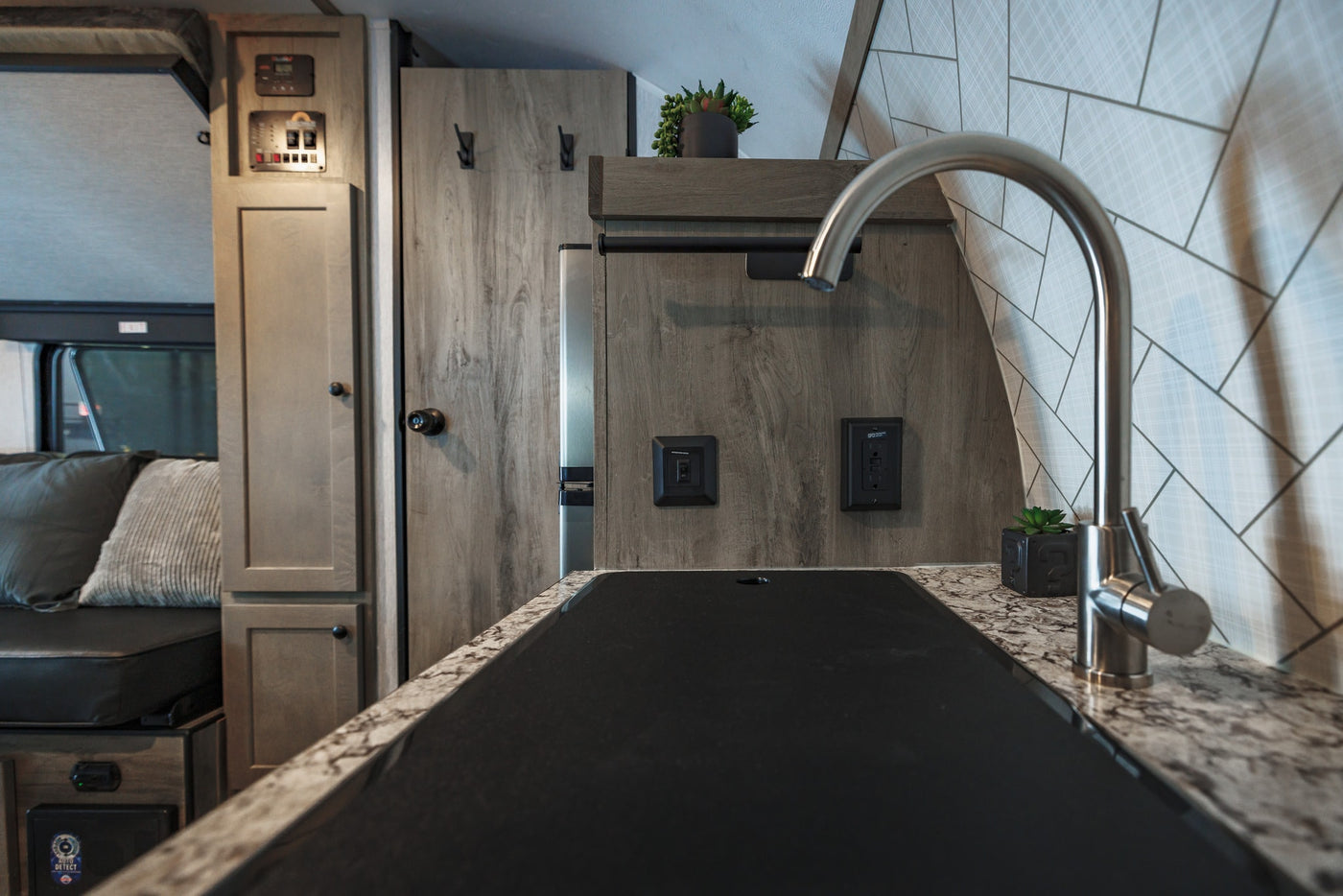 Modern RV rental kitchen with sleek sink, marble-look counter, wood-grain cabinets, and comfortable seating. — photo 18