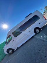 A white Coachmen Galleria L3 RV rental van is brightly lit by the sun on a clear day, parked on asphalt with a green wall behind it.