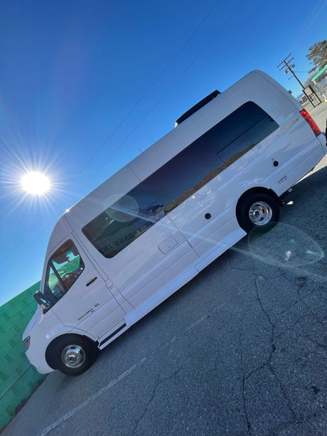 A white Coachmen Galleria L3 RV rental van is brightly lit by the sun on a clear day, parked on asphalt with a green wall behind it.