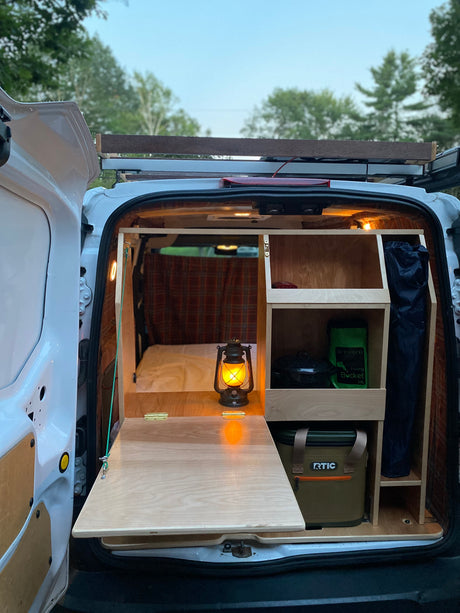 Inside this RV rental campervan, a custom wood build features a fold-out table, bed, and storage shelves with camping gear.