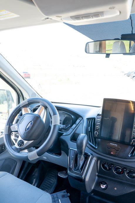 Inside a modern **rv rental** van: driver's cockpit with Ford steering wheel, dashboard, and large display screen.