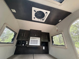 Inside a compact RV rental: featuring windows, overhead fan, AC, and dark wood cabinetry over the bed area.