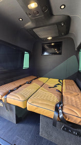 RV rental van interior with three tan quilted seats/beds, seatbelts, wall-mounted TV, and overhead lighting.
