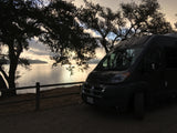 Experience serene travel with an RV rental: dark van by a tranquil lake, silhouetted trees at dawn.