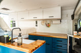 RV rental interior featuring a stylish kitchen with blue cabinets, wood counters, white subway tile, a sink, and a comfy bed.