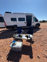 Enjoying outdoor dining with an RV rental. A white Winnebago Solis camper van set up for camping on rocky terrain under a clear sky.