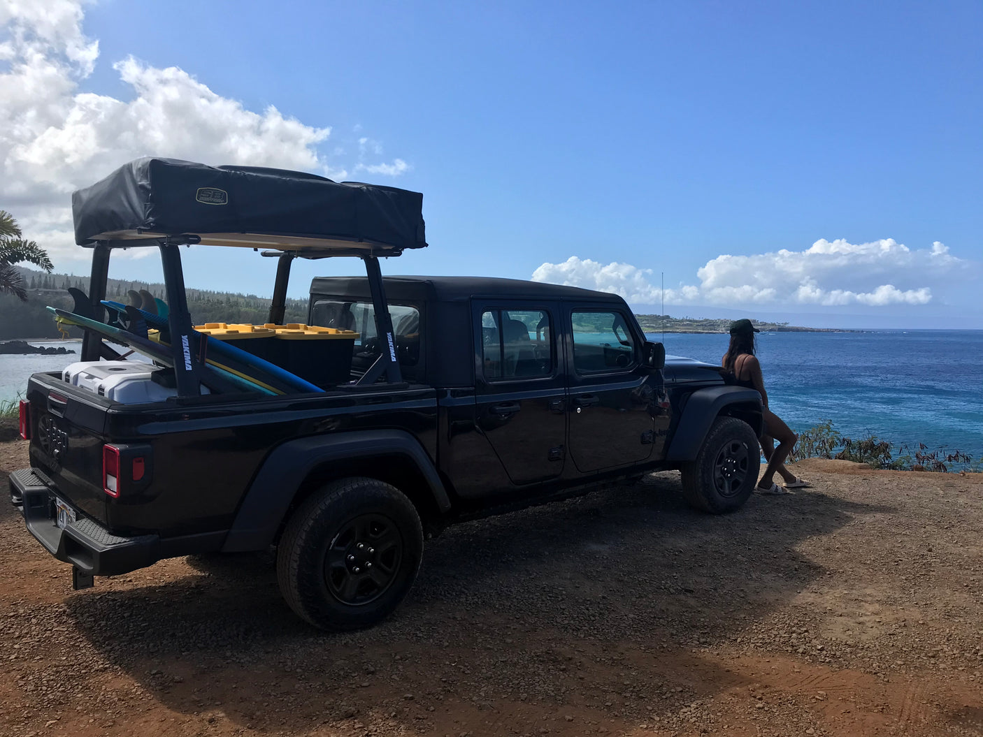 Adventure-ready Jeep Gladiator with rooftop tent and surfboards at scenic coastal overlook. Perfect RV rental for ocean views.