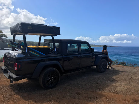 Adventure-ready Jeep Gladiator with rooftop tent and surfboards at scenic coastal overlook. Perfect RV rental for ocean views.