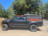 This black overlanding Toyota Tacoma pickup truck with a pop-top camper, ideal for RV rental adventures, is ready for off-road camping.