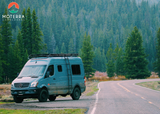 Blue Moterra camper van parked on a winding road amidst a dense forest, ideal for your next rv rental adventure.