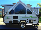 This A-Liner A-frame pop-up camper, an ideal RV rental, features a distinct grey triangular design with large windows, visible outdoors.