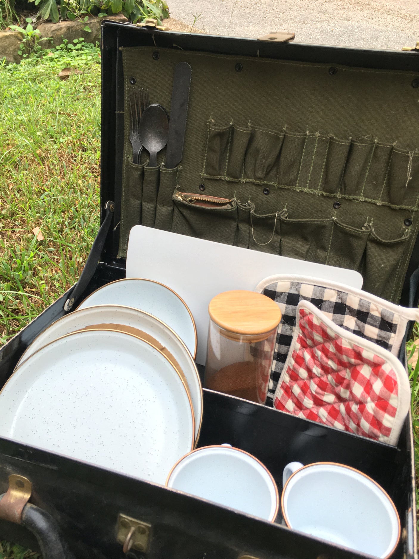 Essential camping kitchenware for your rv rental: plates, utensils, mugs, and pot holders neatly packed in a travel case.