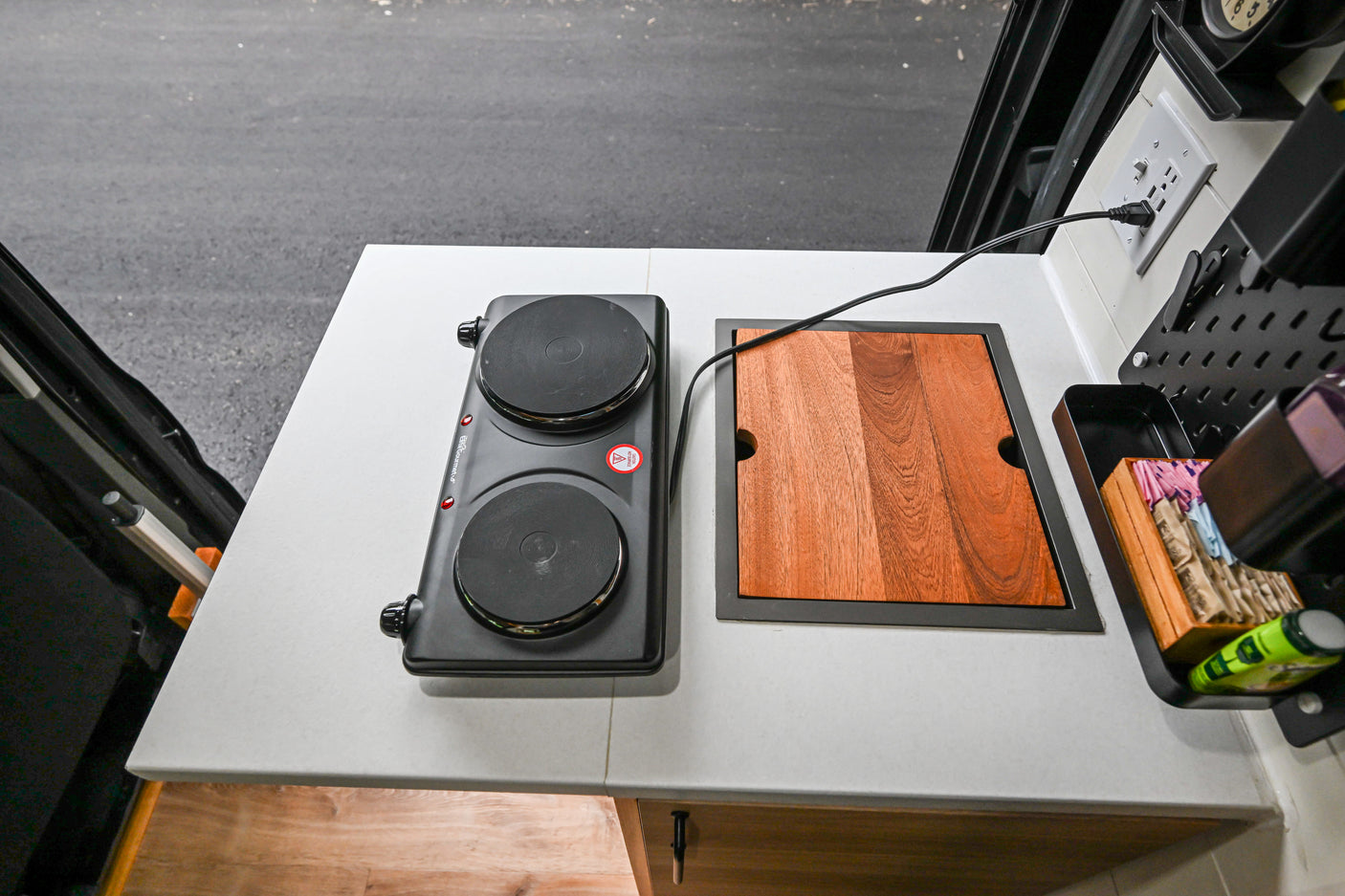 RV rental: Portable double burner and integrated cutting board on a compact counter, ideal for camper kitchens.