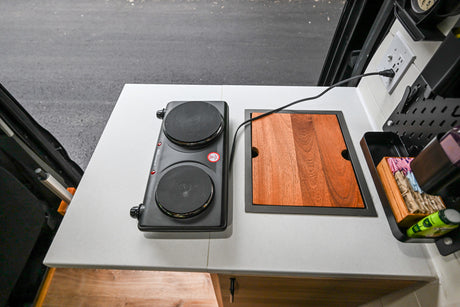 RV rental: Portable double burner and integrated cutting board on a compact counter, ideal for camper kitchens.